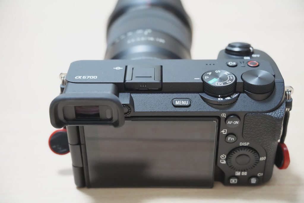 SONY α6700の背面上部を後ろから撮影し、ファインダー、ダイヤル、背面モニターを確認できる様子